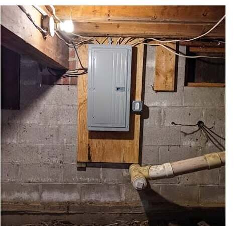 After: a new circuit-breaker load center mounted on a plywood backer board in the same location, with the branch circuits re-run and supported up into the floor joists.