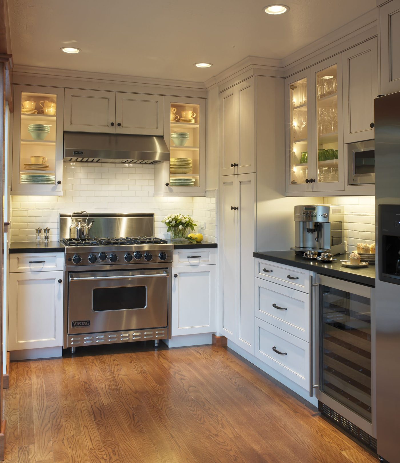 A finished residential kitchen with recessed ceiling lighting, under-cabinet lighting and lit glass-front cabinets.